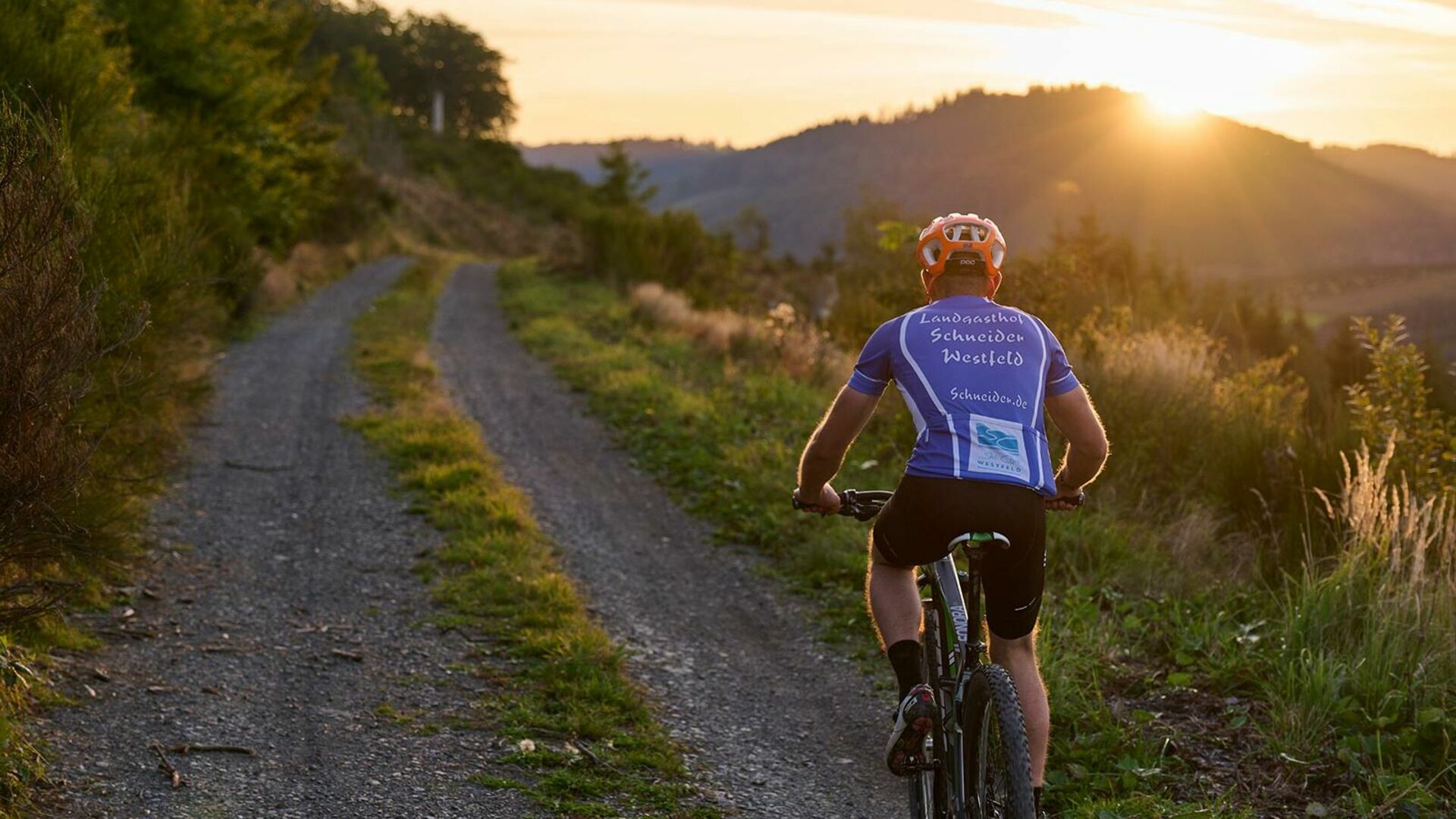 Mann fährt Mountainbike, Sonnenuntergang im Hintergrund